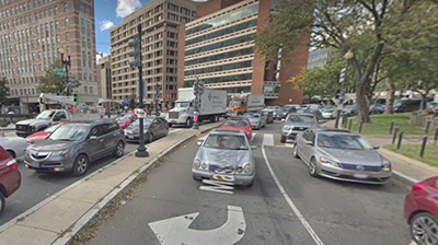 Image of a very large traffic circle with 3 to 4 lanes traveling around it with heavy vehicle traffic and park in center (Dupont Circle, Washington DC).